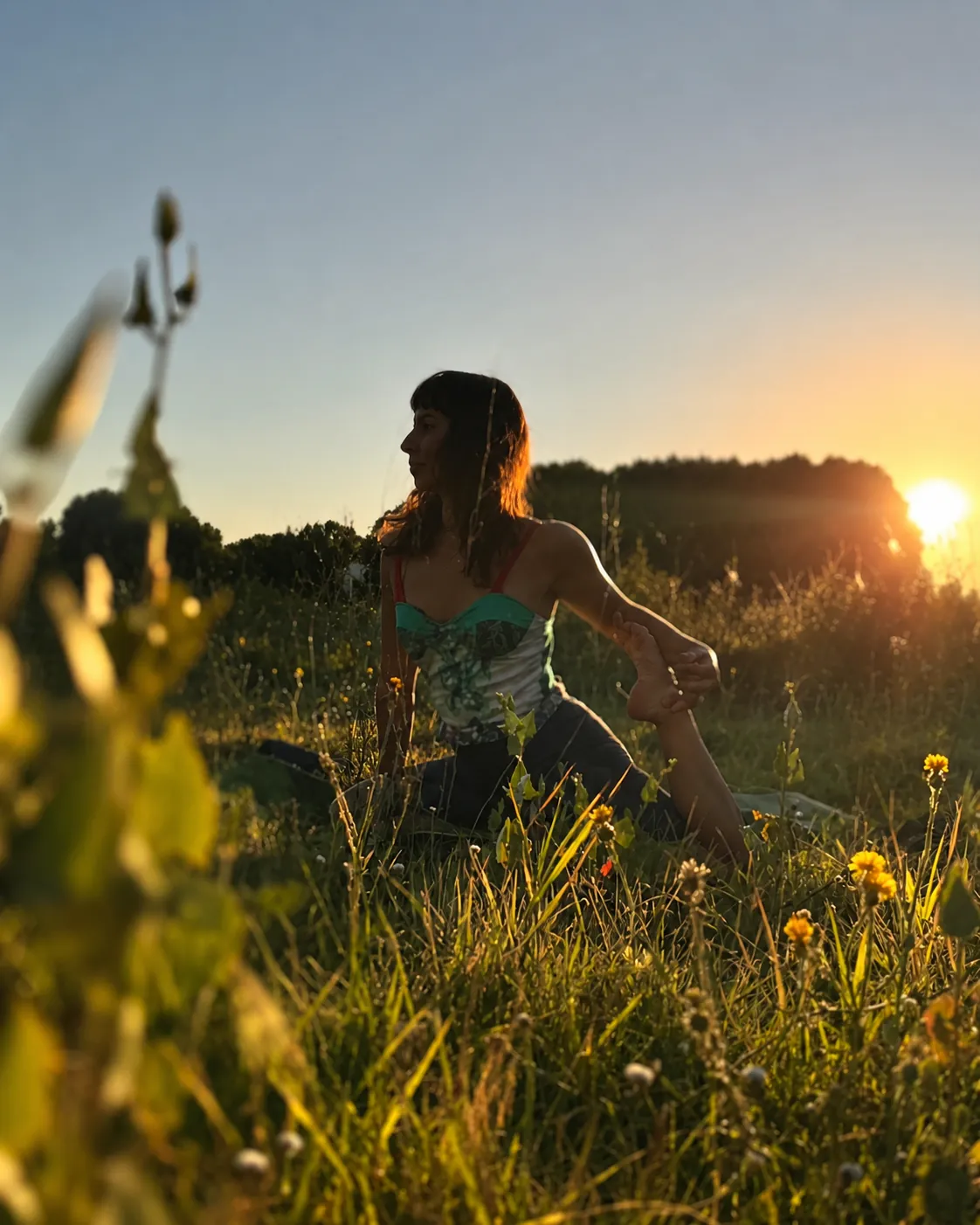 Alumna en postura de yoga en un campo, al atardecer